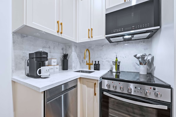 A modern kitchen with white cabinets, a coffee maker, a sink, and a stove.