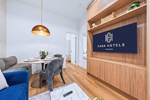 A modern room with a dining table set, a blue sofa, a grey armchair, a wooden cabinet, and a mounted TV displaying 'Casa Hotels Toronto'.