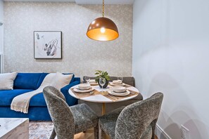 Un comedor con una mesa redonda para cuatro personas, un sofá azul y una lámpara colgante.