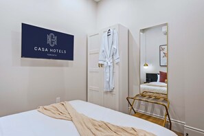Habitación de hotel con una cama, una bata colgada en la puerta, un espejo y un cartel con el nombre del hotel.