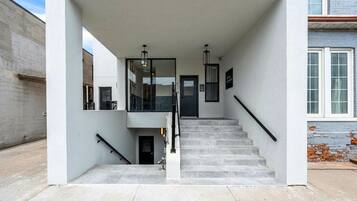 Una entrada moderna de edificio con escaleras, puerta de cristal y barandilla de metal.