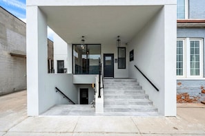 A modern building entrance with a staircase, a glass door, and a metal railing.