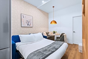 A modern bedroom with a bed, a sofa, a dining table, and a pendant light.