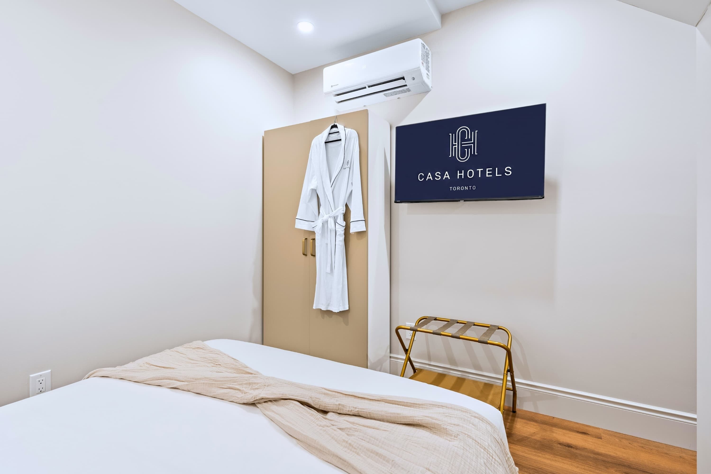 Habitación de hotel con cama, bata colgada en la puerta, toallero y equipo de aire acondicionado.