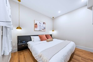A modern bedroom with a large bed, bedside tables, a hanging light fixture, and a wall-mounted artwork.