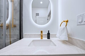 Une salle de bain avec un lavabo blanc, des robinetteries dorées, une douchette à main et un porte-serviettes.