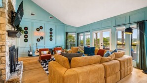 A living room with a large sofa, two armchairs, a fireplace, a guitar, and a wall with vinyl records. - The Lakeside Soundtrack | Pool, Hot Tub, Games (Spicewood)