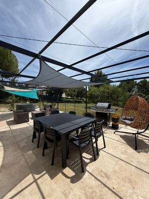 Une terrasse extérieure avec une table et des chaises, un barbecue et un fauteuil suspendu.
