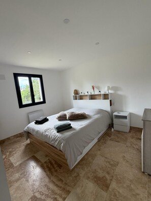 Une chambre à coucher comprenant un lit, une table de chevet, une étagère avec des objets décoratifs et une fenêtre.