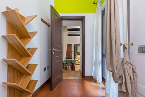 A hallway with a wooden shelving unit, an open door leading to a dining area, and a robe hanging on a hook. - GuestHost - Domus Genovesi Apartment in Casteddu (Cagliari)