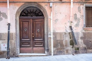 A double wooden door with a decorative arch above it, set in a building with stone and plaster walls. - GuestHost - Domus Genovesi Apartment in Casteddu (Cagliari)