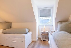 Een slaapkamer met schuin dak, een radiator, een raam met jaloezieën en een bed met hoofdeinde.