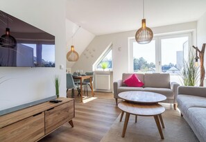 Een moderne woonkamer met een eetgedeelte, een bank, een salontafel en een aan de muur bevestigde televisie.