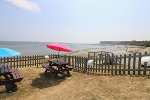 Ein Picknickbereich am Strand mit Holzbänken und Picknicktischen, einem Holzzaun und Blick aufs Meer.