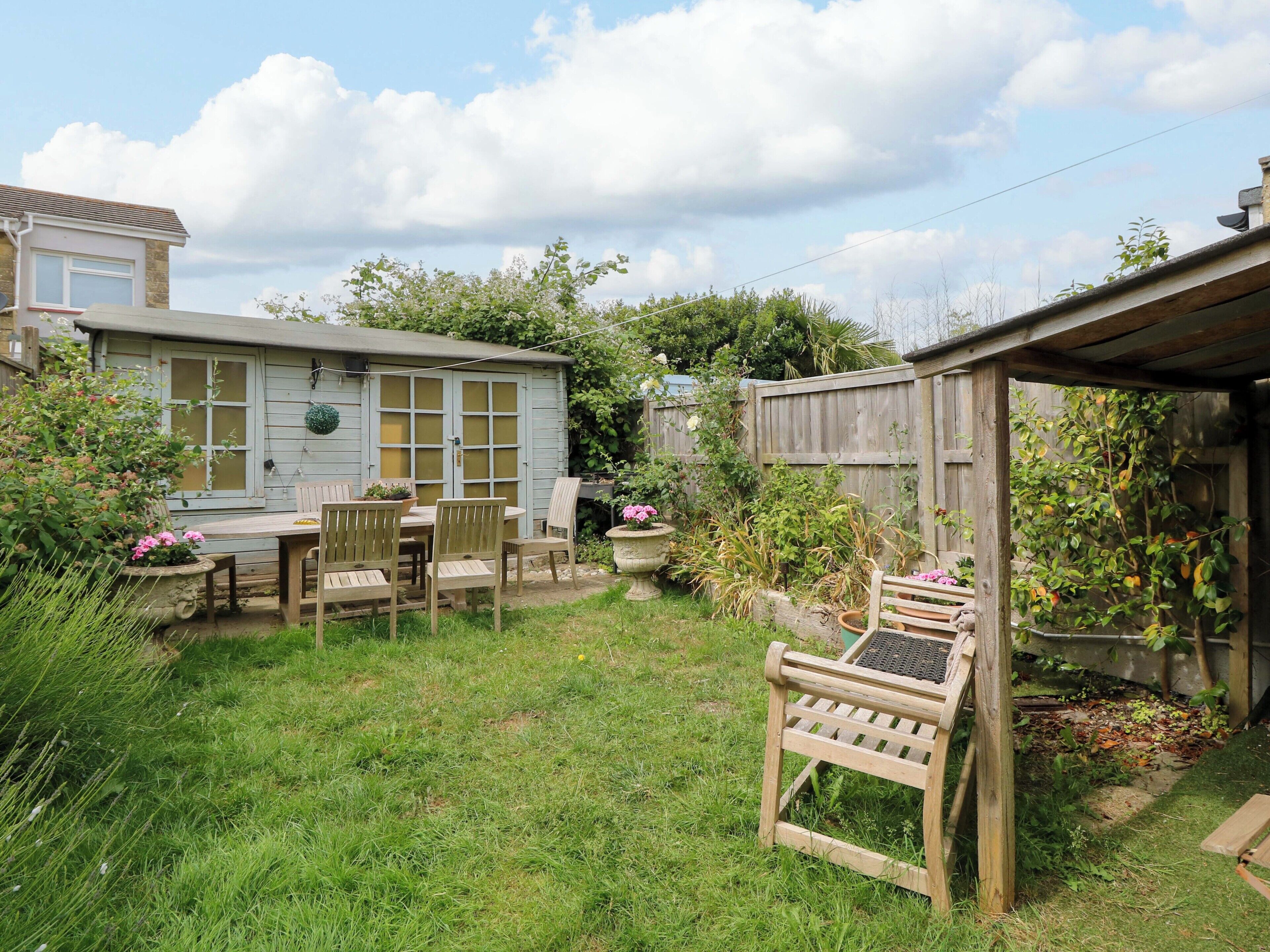 A rustic wooden house with a garden patio, a wooden fence, and various plants.