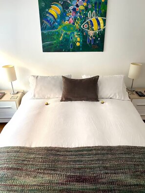 Ein Hotelzimmer mit einem großen Bett, zwei Nachttischen, einer Lampe auf jeder Seite, einem Gemälde über dem Bett und einer gemusterten Tagesdecke.