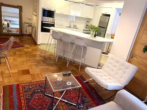 Eine moderne Küche mit weißen Schränken, einer Bar mit Hockern, einem Glastisch und einem weißen Sofa.