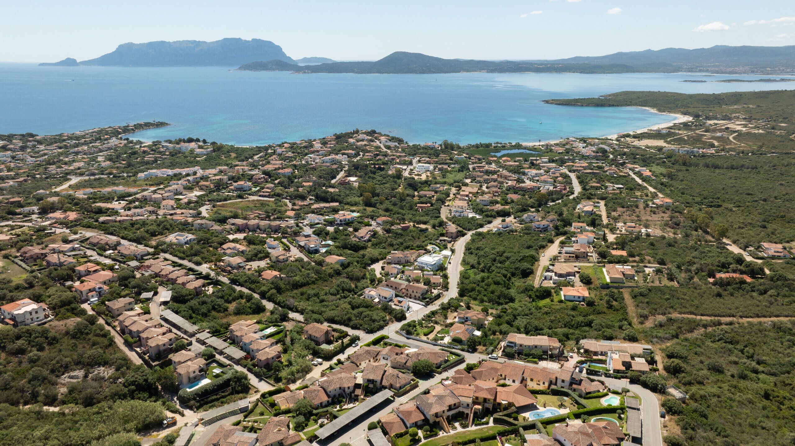 An aerial view of a coastal residential area with houses, roads, and a large body of water.