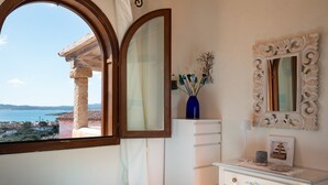 A bedroom with a view of the sea, a wooden column, a white dresser, and a decorative mirror. - Casa dell'Erica by Wonderful Italy (Olbia)