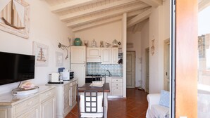 A kitchen with white cabinets, a dining table, and a TV. - Casa dell'Erica by Wonderful Italy (Olbia)