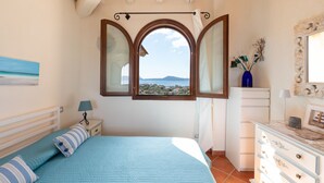 A bedroom with a bed, a dresser, a nightstand, and a window with a view of a landscape. - Casa dell'Erica by Wonderful Italy (Olbia)