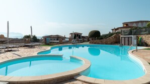 A swimming pool with a curved design, surrounded by stone tiles and a stone wall. - Casa dell'Erica by Wonderful Italy (Olbia)