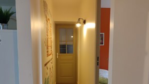 A narrow hallway with a tiled floor, a door with a window, and a wall-mounted light fixture. - The Bicentennial Linden Cottage (Pernes-les-Fontaines)