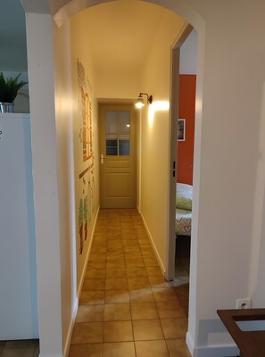 Ein schmaler Korridor mit Fliesenboden, einer Tür mit Fenster und einer Wandleuchte.