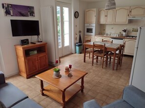 Ein gemütlicher Wohnraum mit Esstisch, Stühlen, einem Fernseher, einem Holzschrank und einer Küchenzeile mit Schränken und Geräten.