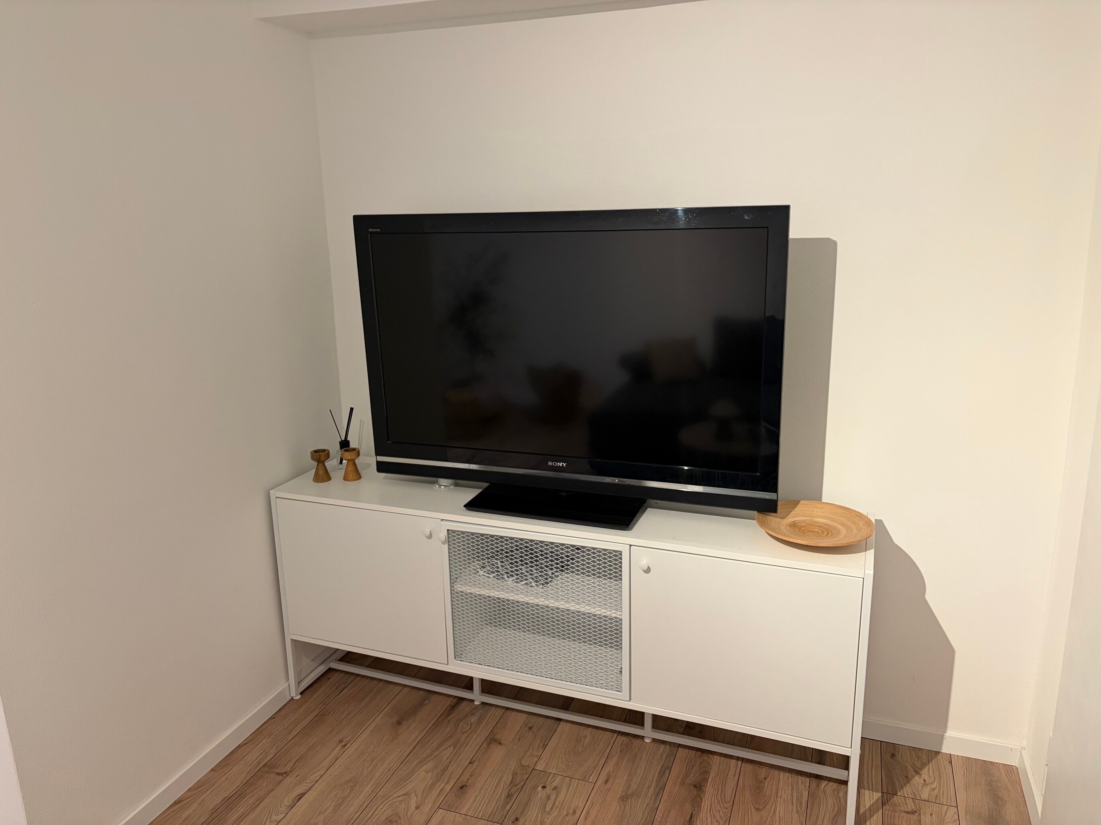 Un téléviseur à écran plat posé sur un meuble de télévision blanc, doté d’un panneau frontal en treillis métallique.