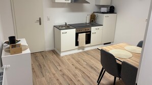 Una cocina compacta con estufa, horno y lavamanos, una mesa de comedor con sillas y un reloj en la pared.