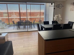 Un intĂ©rieur moderne comprenant un coin repas, un comptoir dâaccueil et une vue sur un espace extĂ©rieur accessible par une porte-fenĂȘtre coulissante.
