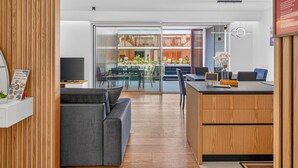 Un espace de bureau moderne avec un canapé gris, un lambris en bois, une porte vitrée donnant sur un espace extérieur et un bureau avec un ordinateur.