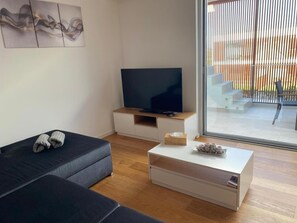 A modern living room with a sofa, a flat-screen TV, a coffee table, and a sliding glass door leading to an outdoor area.