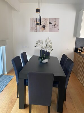A modern dining area with a rectangular table, six chairs, a vase with white flowers, abstract wall art, and a pendant light.
