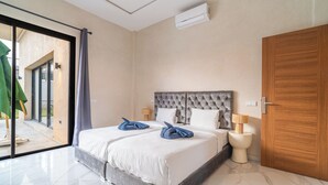 Habitación de hotel con una cama grande, una puerta de madera, una puerta corredera de vidrio hacia el exterior y un aire acondicionado montado en la pared.