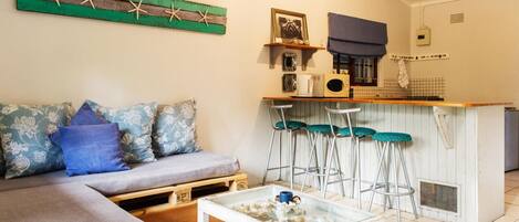 A compact living space with a sofa, a coffee table, a kitchenette, and a bar area.