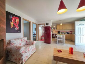 A living room with a sofa, a wooden table, and a kitchen area with cabinets and a refrigerator.
