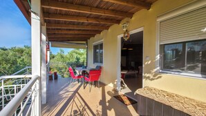 Una veranda coperta con tavolo e sedie, soffitto in legno e vista sugli alberi.