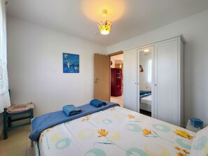 Ein Schlafzimmer mit Bett, Schrank, Tür, einem kleinen Tisch und einer Wand mit einem Gemälde.