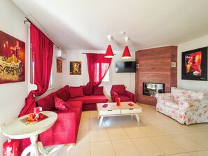 Un salon avec des canapés rouges, une table basse blanche et un téléviseur fixé à un mur en briques.