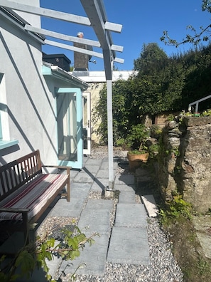 Une terrasse avec un banc, une pergola et un mur en pierre.