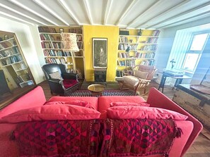 Un salon chaleureux avec un canapé rouge, un fauteuil noir et un mur jaune orné d’étagères.