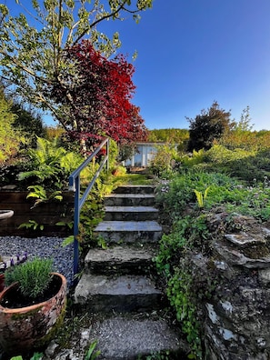 Un escalier en pierre mène à une maison entourée d’une végétation luxuriante et de différentes espèces de plantes.