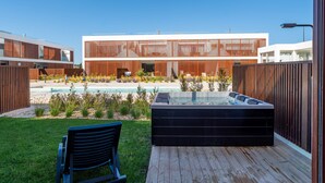 Ein moderner Poolbereich im Freien mit Whirlpool, einer Holzterrasse und einem Gebäude mit großen Fenstern und einer Holzfassade.