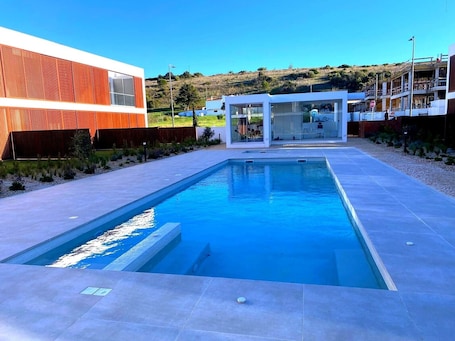 A modern swimming pool with a clear view of the surrounding buildings and a hilly landscape in the background.. Magnolia – Your Holiday Retreat in Burgau