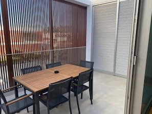 A balcony with a wooden table and chairs, a sliding glass door, and a view of the cityscape.