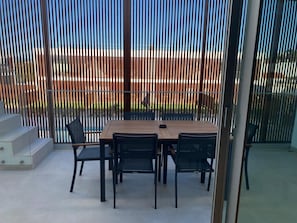 Une terrasse avec une table et des chaises, une porte vitrée et une vue sur une clÎture et de la verdure.
