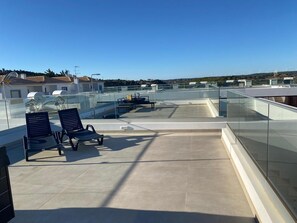 Une terrasse sur le toit, dotĂ©e de rampes en verre, de deux fauteuils et dâune table.