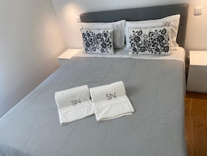 A neatly made bed with two folded towels and two pillows with floral patterns.